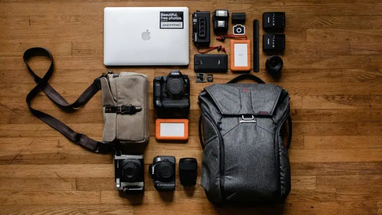High-quality travel tech gear and camera equipment laid out on wooden floor, including laptops, cameras, batteries, SD cards, and a backpack, ideal for tech-savvy travelers and digital nomads.